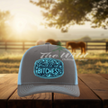 Gray and blue cap with text on a wooden surface with a blurred background of horses and trees.