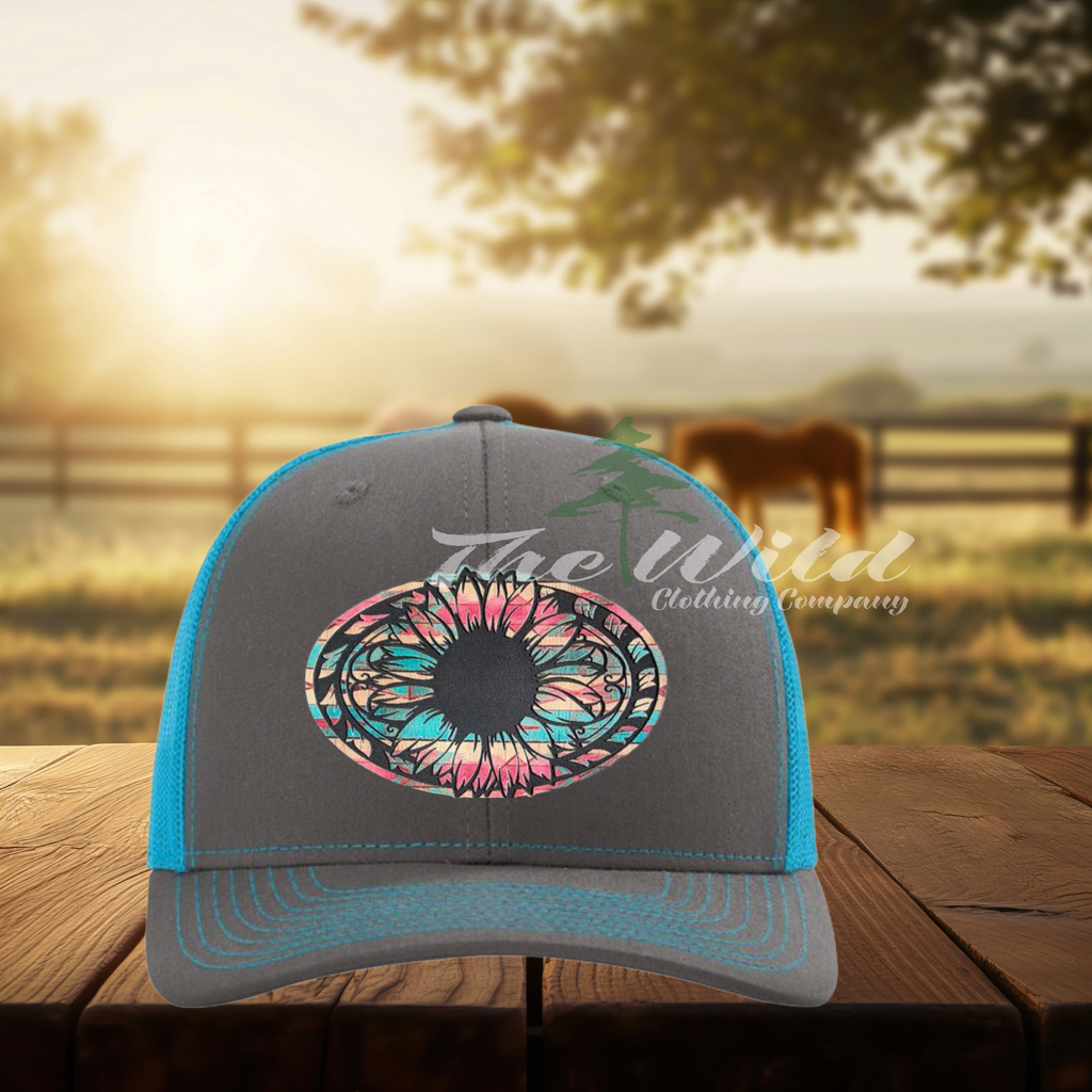 Gray and blue cap with a colorful  sunflower design on a wooden surface with a blurred outdoor background.