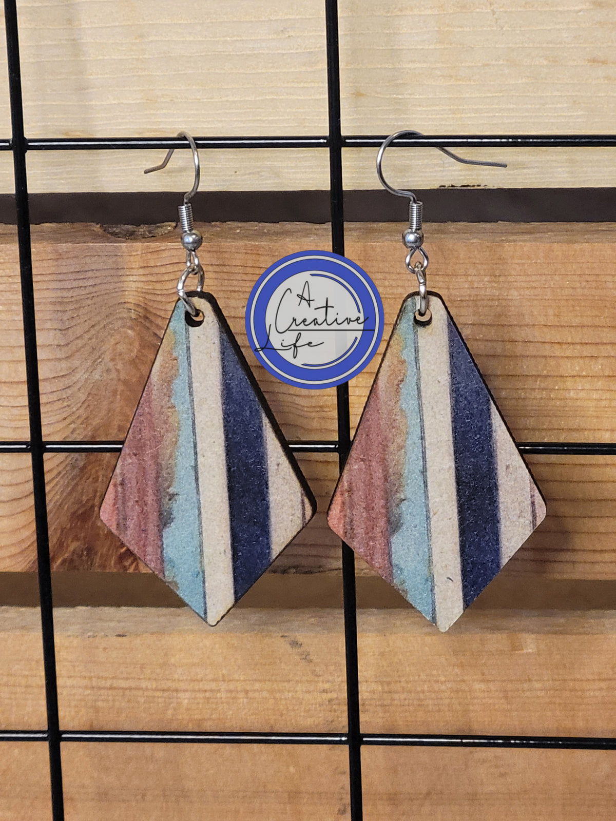 A pair of striped drop earrings with stainless steel plated hooks and an 18K white gold finish, displayed on a wooden hanger.
