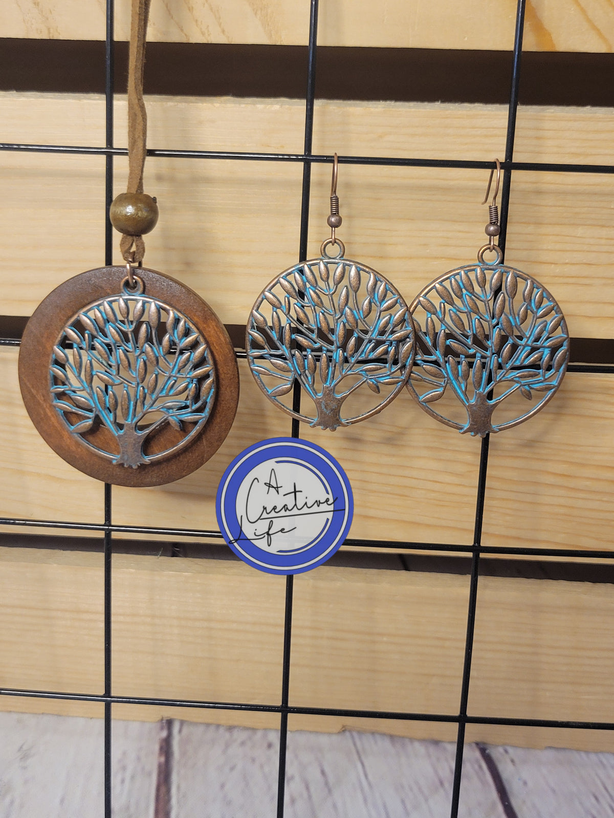 A set of jewelry featuring a wooden necklace with bronze Tree of Life pendants and matching earrings, displayed on a wooden background.