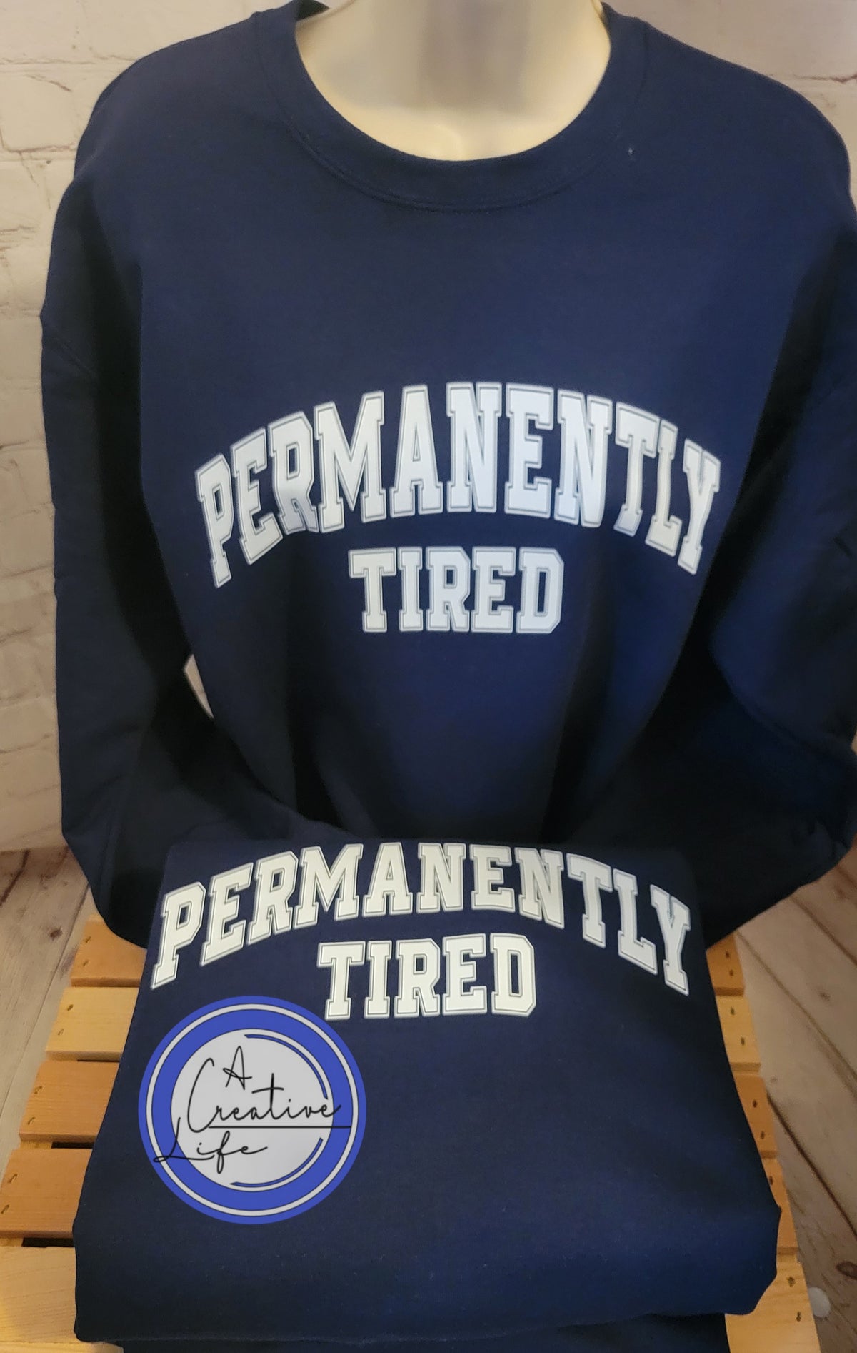 A navy blue sweatshirt with the text 'PERMANENTALLY TIRED' printed in white capital letters on the front.