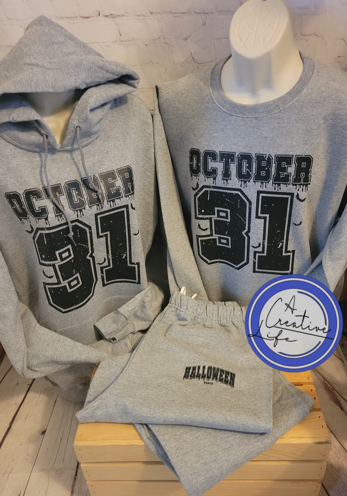 A set consisting of a gray hooded sweatshirt with 'OCTOBER 31' text on the front and matching gray sweatpants with Halloween vibes, displayed on mannequin busts.