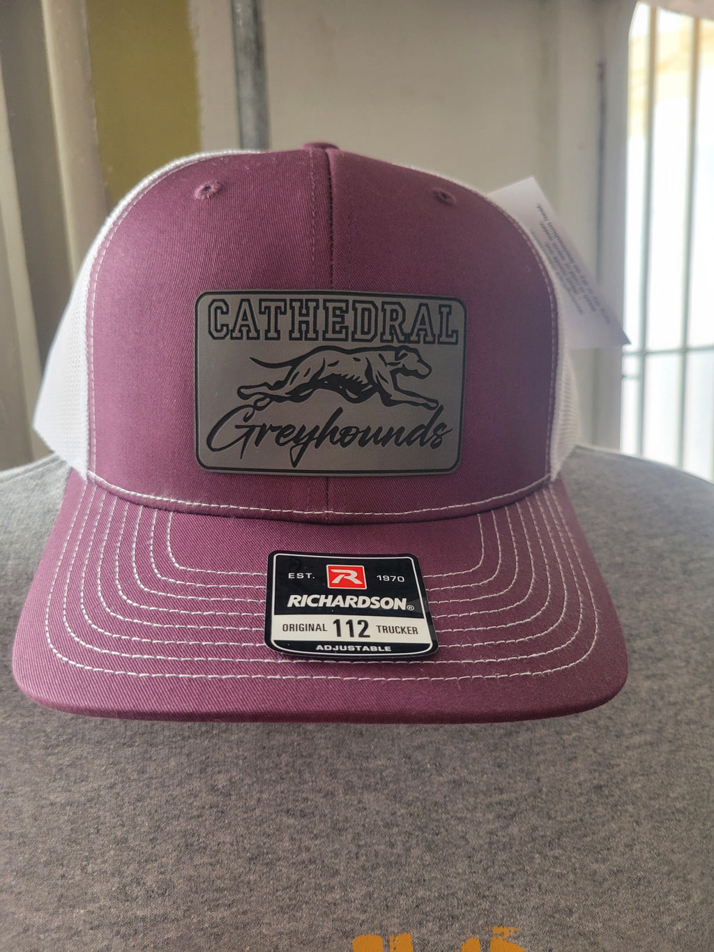 A Richardson 112 trucker hat in a dusty rose/maroon color with white stitching, featuring a grey rectangular patch on the front with a greyhound graphic and the text 'CATHEDRAL Greyhounds'. The back of the cap is white mesh.
