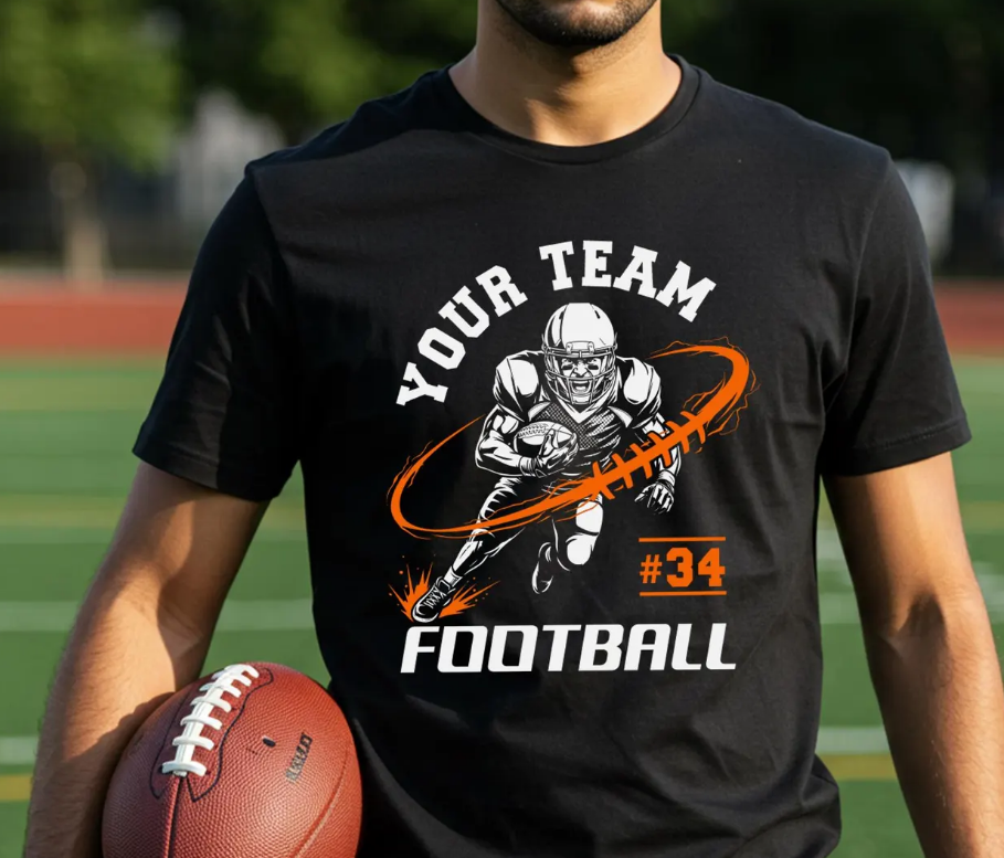 A man wearing a black graphic t-shirt with a football player design and the words 'YOUR TEAM FOOTBALL' and '#34', holding a football on a sports field.