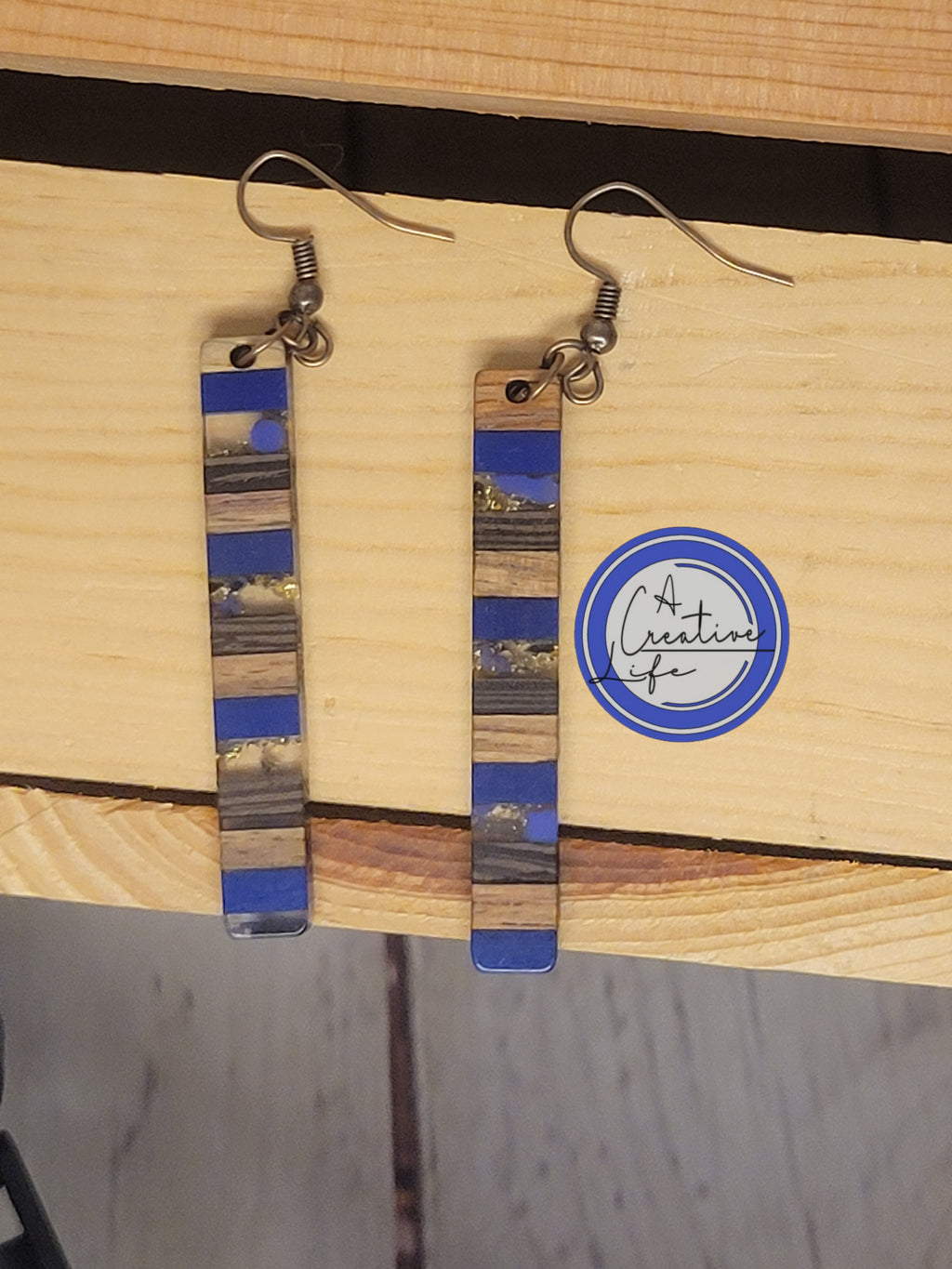 A pair of walnut and blue poly resin drop earrings displayed on a wooden surface.