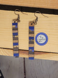 A pair of walnut and blue poly resin drop earrings displayed on a wooden surface.