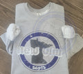 Folded gray t-shirt with a graphic New Ulm 56073 design on a wooden surface