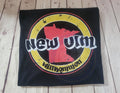 Black t-shirt with a red and yellow New Ulm Willkommen graphic design on a wooden surface