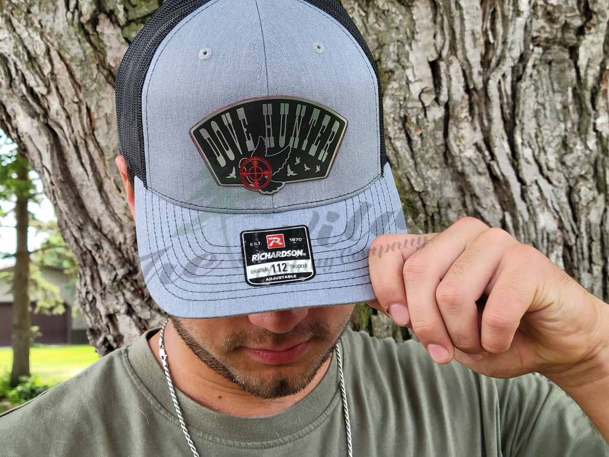 Person wearing a cap with a logo and text, standing against a tree.