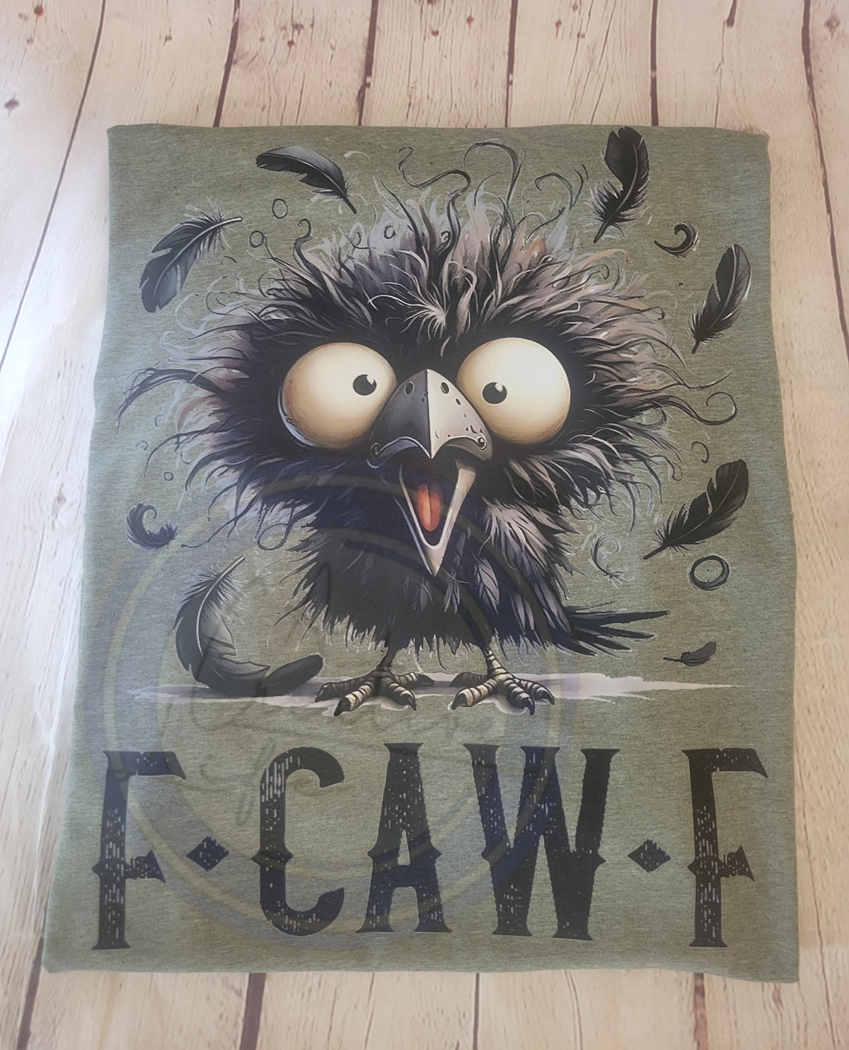 Illustration of a cartoon crow with large eyes and feathers on a green tshirt