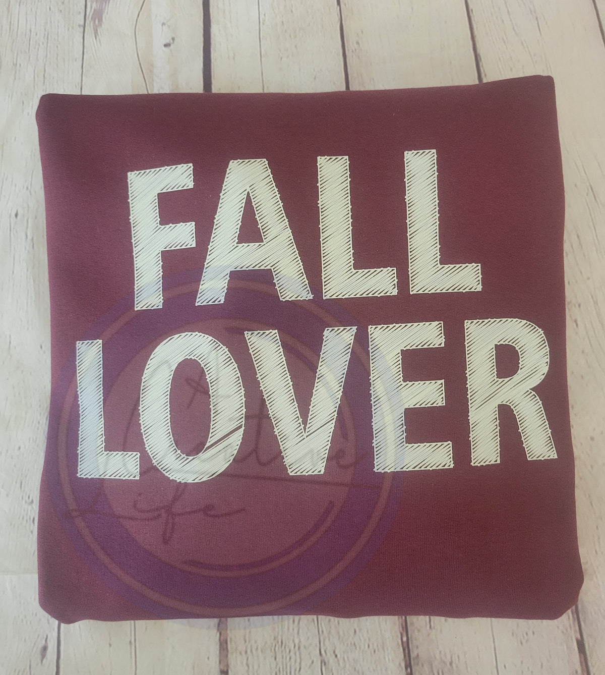 Maroon sweatshirt with 'FALL LOVER' text on a wooden surface