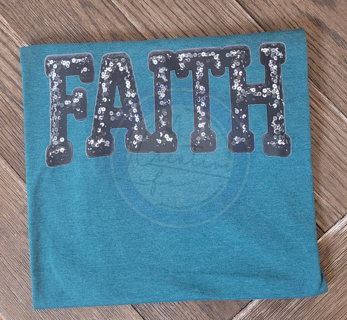 Teal fabric with 'FAITH' in sequin letters on a wooden surface