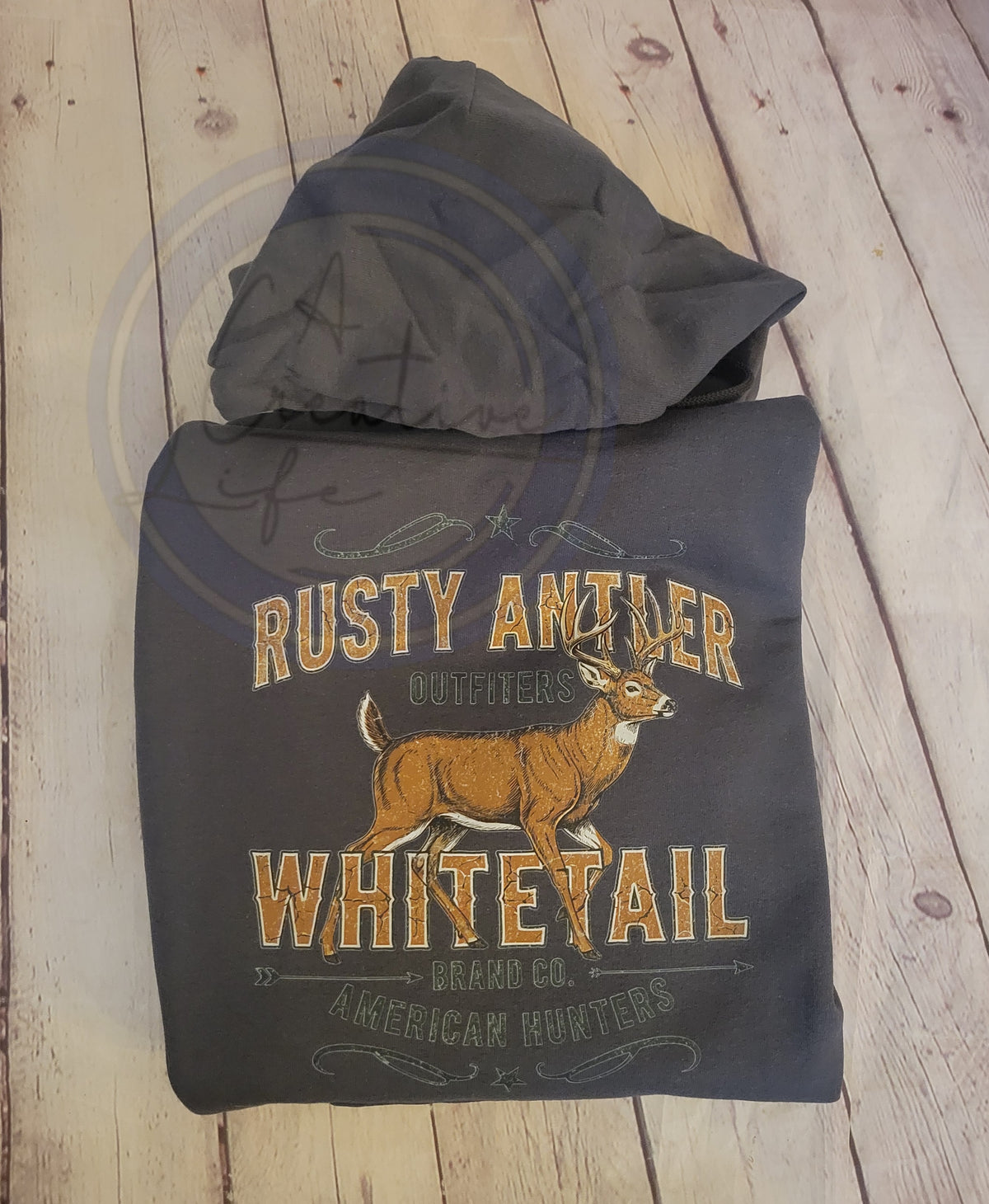 Hoodie with 'Rusty Antler Whitetail' design on a wooden surface