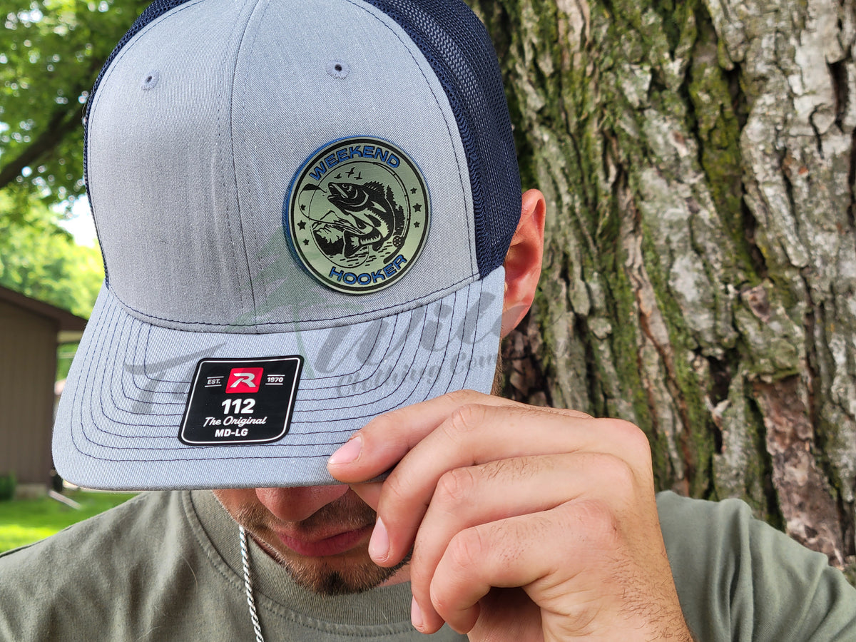 Person wearing a gray and navy cap with a logo, adjusting it against a tree background.