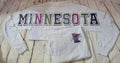 Gray sweatshirt with 'MINNESOTA' in colorful letters on a wooden surface