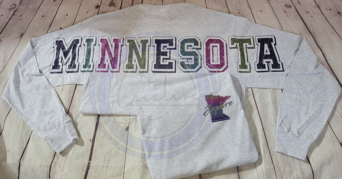 Gray sweatshirt with 'MINNESOTA' in colorful letters on a wooden surface