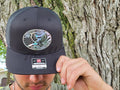 Person holding a black cap with a holographic 250 years American eagle decorative emblem against a tree background