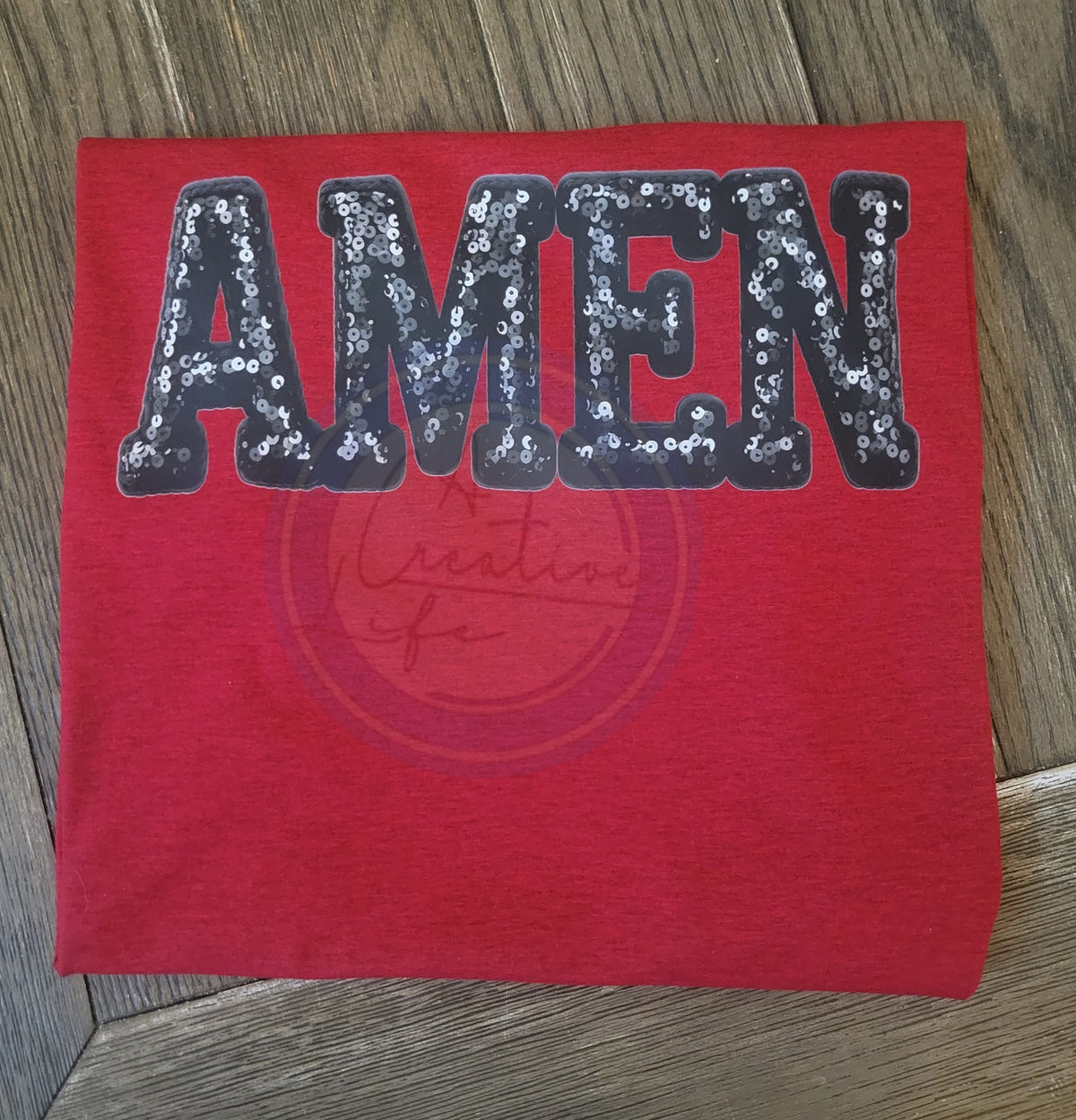 Red fabric with 'AMEN' in sequins on a wooden surface