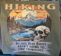 T-shirt with a mountain and skull design and text 'Hiking because dead bodies aren't going to find themselves' on a green background.