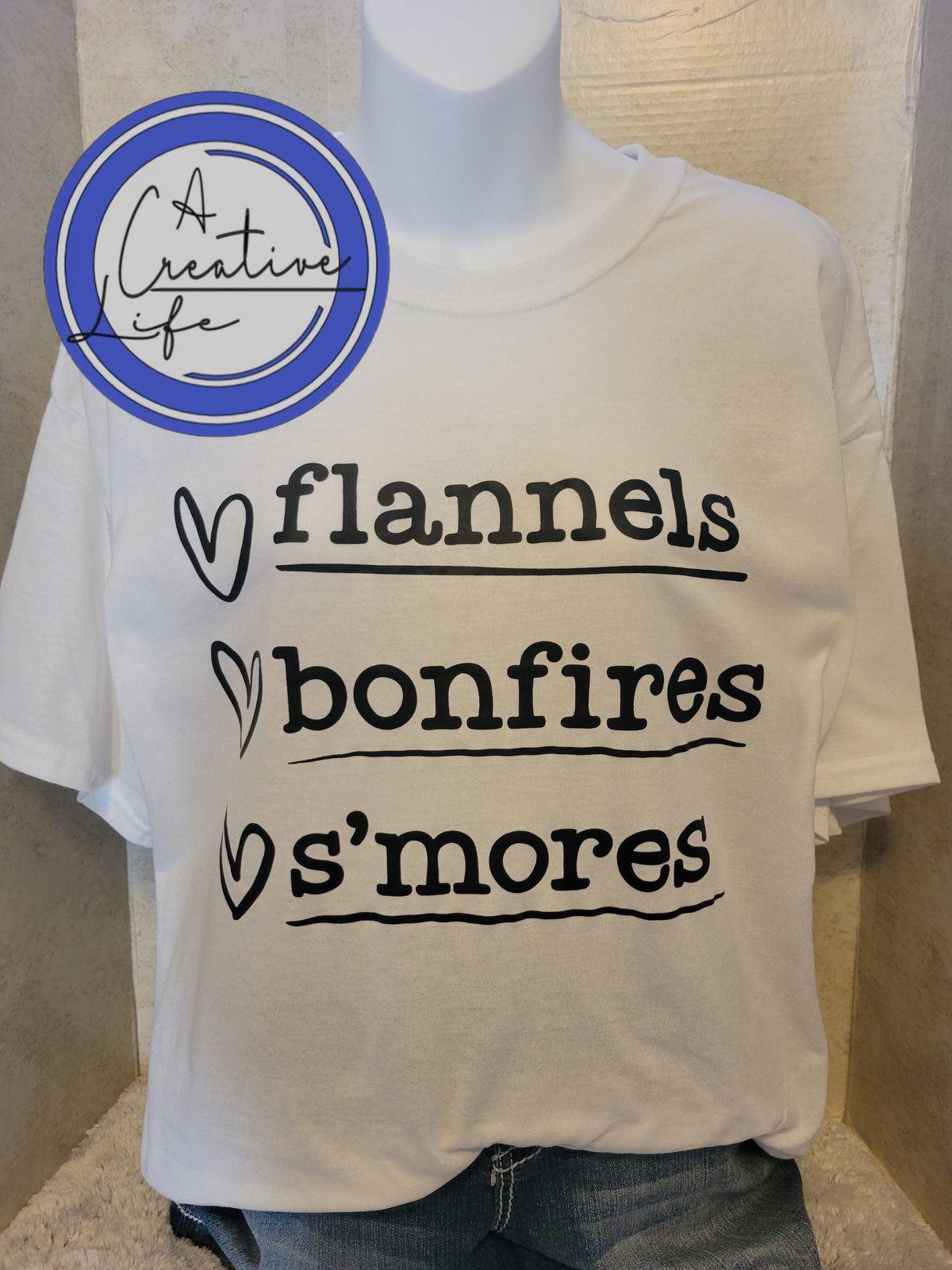 White tshirt displaying flannels, bonfires, s'mores on a mannequin.